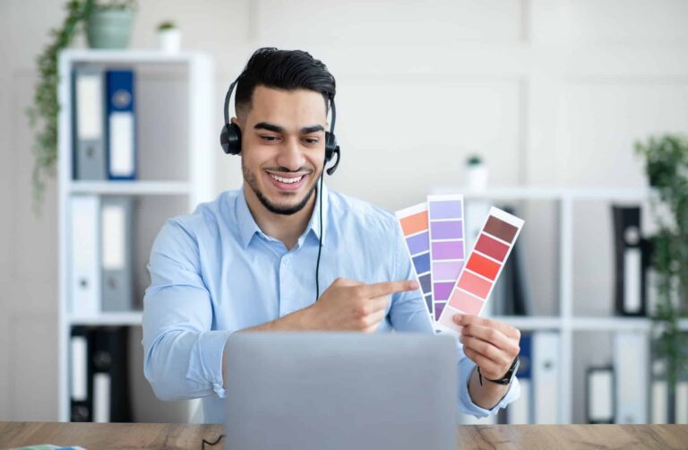 Arab man holding color swatches in front of laptop at office presenting graphic design project.jpg