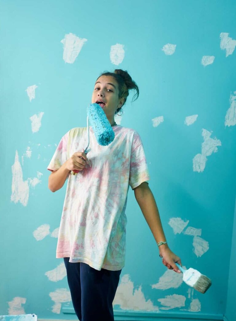 Happy woman painting interior wall with paint roller in new house e1678323493469.jpg