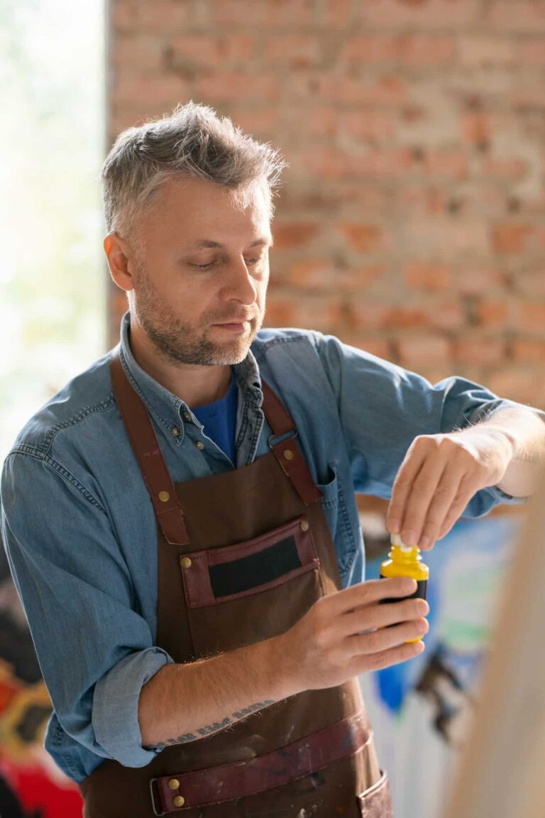 Mature painter in workwear uncovering plastic jar with gouache.jpg